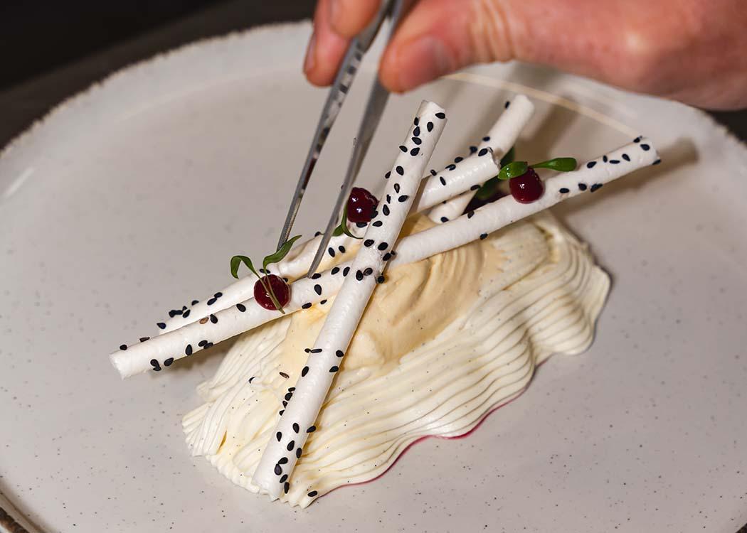 Un chef añadiendo con pinzas los últimos detalles de un postre