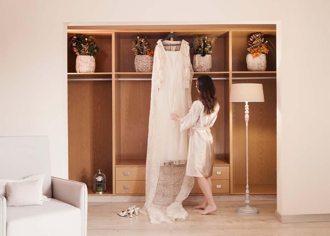 Una novia admira su traje de boda colgado en una percha en un amplio vestidor